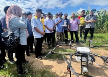 MOHAMAD Sabu (enam dari kanan) meninjau dron yang digunakan bagi tujuan penyemburan racun sewaktu Lawatan Kerja Ke Projek Tanaman Jagung Bijian di Lembah Chuping, Padang Besar, Perlis hari ini. -UTUSAN/ASYRAF MUHAMMAD