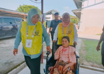 PETUGAS SPR membantu menyorong kerusi roda Munah Adam ketika keluar mengundi di SK Pasir Raja, Hulu Dungun, Dungun, hari ini. - UTUSAN/NIK NUR IZZATUL NIK ADNAN 