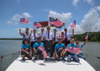 MUSTAFA Abdul Wahab (berdiri, tengah) bersama kru kapal KKN Sea Hunt turut mengibarkan Jalur Gemilang sempena bulan kemerdekaan ketika program Boat and Tour Go Green Eco Travel with Boat House di Jeti Semeling, Bedong Sungai Petani. -UTUSAN/SHAHIR NOORDIN