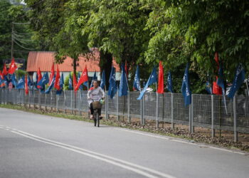 SEORANG warga emas yang menaiki basikal melintasi deretan bendera parti politik yang bertanding PRN di Kedah. -UTUSAN/SHAHIR NOORDIN