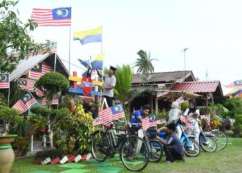 ABDUL Aziz Shaari dan ahli keluarga menghias kawasan kediaman dengan kibaran Jalur Gemilang di Kampung Santan, Kangar, Perlis, semalam. - UTUSAN/IZLIZAN OTHMAN