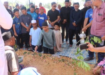 ANAK sulung Allahyarham  Khairil Azwan Jamaludin, Khairul Harisin menyiram air mawar ke atas pusara ayahnya di Tanah Perkuburan Islam Felda Mempaga 1. - UTUSAN/SALEHUDIN MAT RASAD