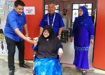 Ahmad Said (berdiri, tengah) bersama isterinya, Norliza Mahmud (kanan) menyorong kerusi roda ibu mertuanya, Selamah Ngah di pusat mengundi di SKTeluk Kalong, Kemaman, hari ini. - UTUSAN/NIK NUR IZZATUL HAZWANI NIK ADNAN