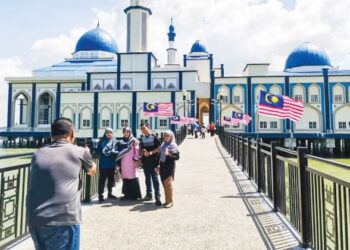 PENGUNJUNG bergambar di laluan masuk ke Masjid Tuminah Hamidi di Bagan Datuk yang dihiasi Jalur Gemilang. – UTUSAN/AIN SAFRE BIDIN