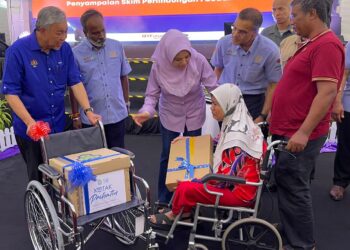 Ahmad Zahid (kiri) menyerahkan sumbangan kerusi roda dan Kotak Prihatin kepada Siti Rokayah Baharum di pekarangan Dewan Millenium, Seberang Perai, Pulau Pinang, hari ini. - MINGGUAN/SITI NUR MAS ERAH AMRAN