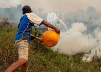 SEORANG petani menggunakan baldi untuk menyimbah air ke kawasan tanah yang terbakar di kampung Soak Batok di Ogan Ilir, Sumatera Selatan.-AGENSI