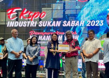 HANNAH Yeoh (tengah) menyampaikan geran padanan sukan kepada salah seorang penerima, sambil disaksikan oleh Menteri Belia dan Sukan Sabah, Datuk Ellron Angin (kanan) di Kota Kinabalu hari ini