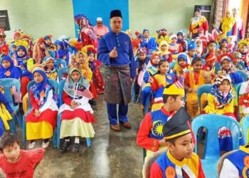 MAT Romli Norman (berdiri tengah) sambil memerhatikan murid segak mengenakan busana tradisional berasaskan Jalur Gemilang sempena sambutan Hari Malaysia dan penutup bulan kemerdekaan di Felda Kota Gelanggi Dua, Jerantut baru-baru ini. – UTUSAN/HARIS FADILAH AHMAD