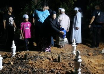 NORIAH Ismail menyiram pusara anak lelaki dan dua cucunya yang maut dalam kemalangan di Tanah Perkuburan Islam Kampung Jabur Kubur, Kemaman, malam tadi. - UTUSAN/NIK NUR IZZATUL HAZWANI NIK ADNAN