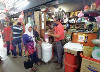 CHONG Chin On (kanan) membungkus beras kilo untuk pelanggan
 di kedainya di Teluk Intan. – UTUSAN/AIN SAFRE BIDIN