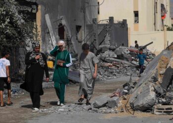 PENDUDUK Palestin berjalan di sebalik bangunan yang runtuh susulan serangan rejim zionis di kem pelarian Rafah di selatan Semenanjung Gaza. – AFP