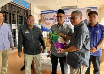 MUHAMMAD Husain (tengah) melakukan gimik penyerahan beras kepada wakil PPK Sri Gunong, Mohd. Radzuan Hamat di Bachok, Kelantan, hari ini. -UTUSAN/TOREK SULONG