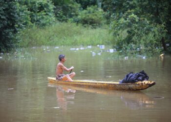 SEORANG penduduk kampung menggunakan sampan untuk bergerak di kawasan rumahnya setelah ditenggelami air banjir di Kampung Tersang, Rantau Panjang.-UTUSAN/KAMARUL BISMI KAMARUZAMAN