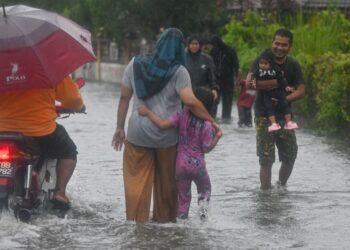 PENDUDUK kampung melalui jalan yang digenangi air berikutan hujan lebat sejak beberapa hari di Kampung Atas Tol, baru-baru ini. -UTUSAN/PUQTRA HAIRRY