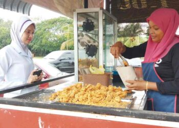 SITI Rahmah Ahmad  melayan pelanggannya yang membeli ayam goreng RM1 di gerainya di Taman Mesra, Kupang, Baling.