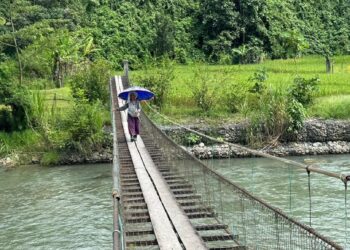 PENDUDUK kampung menaiki jambatan gantung untuk ke kebun yang berada di seberang Sungai Kadamaian.