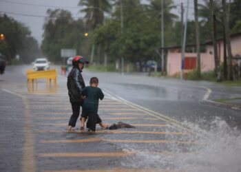 SEORANG penduduk bersama anaknya berusaha mengalihkan sebatang kayu yang dihanyutkan arus air Kampung Dalam Rhu, Pasir Putih, Kelantan hari ini-UTUSAN/KAMARUL BISMI KAMARUZAMAN