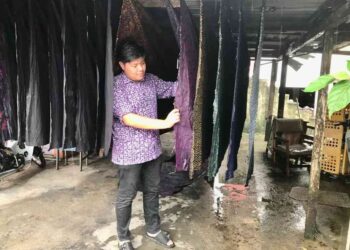 MUHAMMAD Fadhillah Ibrahim melihat kain pasang batik yang dijemur di bangsal rumahnya di Kampung Sungai Keladi, Kota Bharu, Kelantan.- UTUSAN/ROSLIZA MOHAMED.