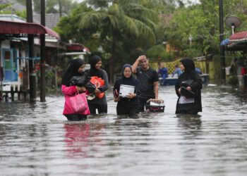 SEBAHAGIAN penduduk meredah banjir dengan membawa barangan keperluan untuk berpindah di Taman Murni Permai, Tok Jembal, Kuala Nerus, hari ini.- UTUSAN/PUQTRA HAIRRY ROSLI