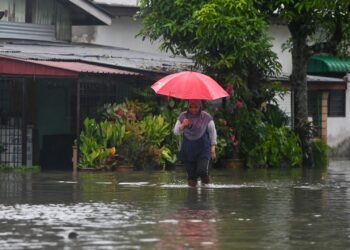 SEORANG penduduk meredah banjir sambil berpayung di Kampung Alur, Surau Panjang, Kuala Terengganu. - UTUSAN/PUQTRA HAIRRY ROSLI   