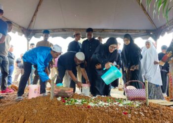 AHLI keluarga menyiram air dan menabur bunga di pusara Allahyarham di Tanah Perkuburan Masjid Al-Abrar, Semabok, Melaka. - UTUSAN/SYAFEEQ AHMAD