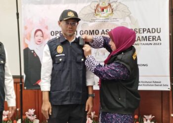 KASEMANI Embong (kanan) memasang kamera badan pada vest anggota penguatkuasa pada Operasi Gomo Asap dan Majlis Penyerahan Vest Penguatkuasaan Berkamera di Klinik Kesihatan Rahmat, Setiu, hari ini. -UTUSAN/WAN ZURATIKAH IFFAH WAN ZULKIFLI