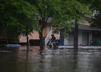 SEORANG penduduk menunggang motosikal sambil mengharungi banjir di Kampung Gong Baru, Kuala Terengganu, hari ini. - UTUSAN/PUQTRA HAIRRY ROSLI