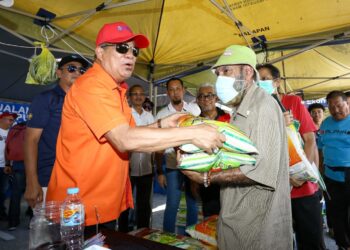 MOHAMAD Sabu menyerahkan beras yang dibeli pelanggan sempena jualan Agro Madani pada Hari Peladang, Penternak dan Nelayan Kebangsaan (HPPNK) di Bulatan Sultan Azlan Shah di Ipoh hari ini. - UTUSAN/MUHAMAD NAZREEN SYAH MUSTHAFA