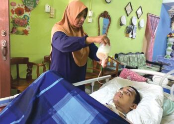 SALBIAH Mohamad Salleh (berdiri) memberikan susu khas kepada Ahmad Fazlan Mohd. Zubir yang mengalami masalah lumpuh di Taman Sungai Karang Darat 2, Kuantan, Pahang.