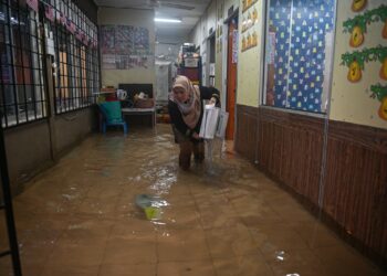 SEORANG guru mengemas buku di sebuah kelas yang dinaiki air di Sekolah Kebangsaan Wakaf Mempelam, Kuala Terengganu, semalam. - UTUSAN/PUQTRA HAIRRY ROSLI