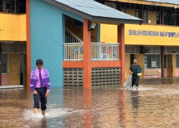 SEORANG murid meredah banjir di SK Wakaf Mempelam, Kuala Terengganu. - UTUSAN/PUQTRA HAIRRY ROSLI