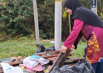 MARINA Husain melihat buku sebahagian buku sekolah dua anaknya yang rosak akibat banjir kilat yang berlaku di Ketengah Jaya, Terengganu. - UTUSAN/NIK NUR IZZATUL HAZWANI NIK ADNAN
