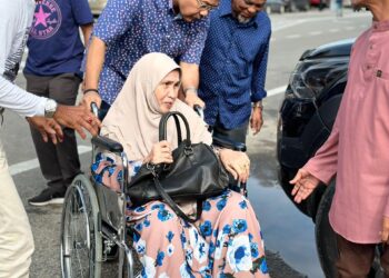 MOHD. SHARKAR Shamsudin (tengah) membantu menolak seorang pengundi PRK Parlimen Kemaman yang menaiki kerusi roda di Sekolah Menengah Kebangsaan (SMK) Geliga, Kemaman.