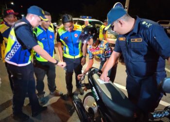 MUHAMMAD FIRDAUS Shariff (kanan) melihat anggota JPJ memeriksa seorang penunggang motosikal di Malim, Melaka. - UTUSAN/AMRAN MULUP