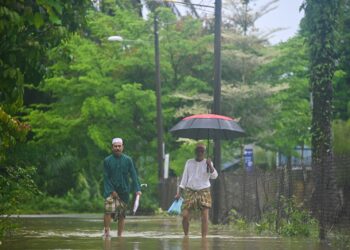 DUA penduduk meredah banjir setelah pulang daripada menunaikan solat Jumaat di Kampung Pengkalan Ajal, Kuala Berang, Hulu Terengganu, semalam. - UTUSAN/PUQTRA HAIRRY ROSLI