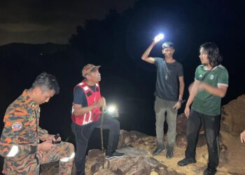 ANGGOTA bomba sedang mendapatkan maklumat untuk membawa turun tiga lelaki yang sesat ketika mendaki Bukit Janda Mandi di Kijal, Kemaman, malam ini. - UTUSAN/NIK NUR IZZATUL HAZWANI NIK ADNAN