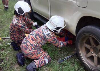 ANGGOTA bomba mengeluarkan penunggang motosikal yang tersepit di bawah kenderaan pacuan empat roda dalam kemalangan di Gerik hari ini.- UTUSAN/IHSAN JBPM