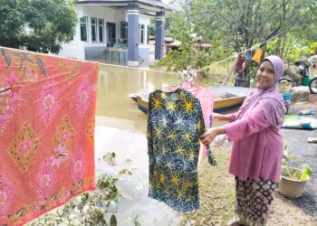 SANAH Ya menjemur pakaian yang dibasuhnya walaupun kawasan rumahnya masih ditenggelami banjir di Kampung Tersang, Rantau Panjang, Kelantan semalam-UTUSAN/ROHANA ISMAIL.