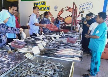 MUHAMMAD Faiz Fadzil (tiga kiri) membantu melayan pelanggan di pasar nelayan milik Persatuan Nelayan Kuala Muda di Kuala Muda di sini hari ini.