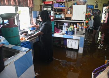 SEORANG penduduk, Azizah Mohammad Hasan sempat memasak walaupun rumahnya dinaiki air dalam kejadian banjir di Kampung Paya, Balai Besar, Dungun, semalam. - UTUSAN/PUQTRA HAIRRY ROSLI