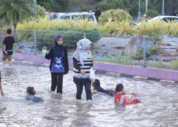 Orang ramai tidak melepaskan peluang bermain air banjir di kawasan persimpangan lampu isyarat Petronas di Rantau Panjang, Kelantan kelmarin. – UTUSAN/KAMARUL BISMI KAMARUZAMAN