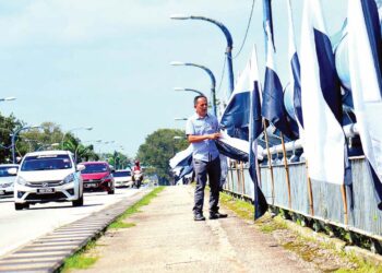 SEORANG lelaki membetulkan bendera negeri Pahang yang dipasang di jambatan Sungai Kuantan di Jalan Tanah Putih di Kuantan, Pahang sempena menyambut keberangkatan pulang Al-Sultan Abdullah dan Tunku Azizah ke Pahang hari ini. – UTUSAN/SHAIKH AHMAD RAZIF