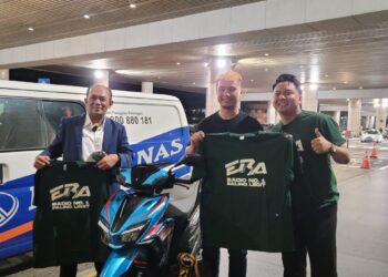 ROSLAN Roskan (kanan) menyampaikan sebuah Modenas Karisma 125S serba baharu kepada peminat bola sepak tular, Derrick Gan di KLIA.