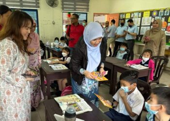 FADHLINA Sidek (dua dari kiri) beramah mesra sambil mengedarkan pelitup muka kepada murid SJKC Yeong Chang di Sungai Suloh, Batu Pahat.