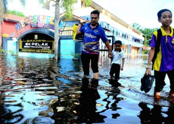 SEORANG guru Sekolah Kebangsaan (SK) Pelak, Zafri Dollah, 45, bersama anak-anaknya mengharung air banjir di pintu masuk dan keluar sekolah terbabit di Kampung Pelak di Pekan, Pahang. - FOTO/SHAIKH AHMAD RAZIF