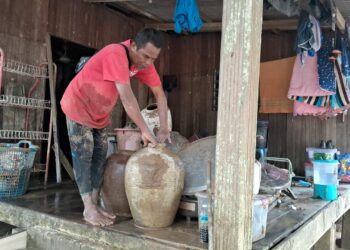 SEORANG penduduk membersihkan perkakasan di rumahnya setelah banjir surut di Kampung Pasir Raja, Hulu Dungun, hari ini. - UTUSAN/NIK NUR IZZATUL HAZWANI NIK ADNAN