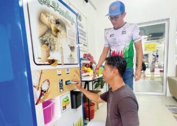 IZIZAM Ibrahim (kanan) meninjau salah seorang pembeli menggunakan mesin beras layan diri di Pusat Khidmat DUN Titi Tinggi, Padang Besar, Perlis yang beroperasi sejak tiga bulan lalu. - UTUSAN/ASYRAF MUHAMMAD