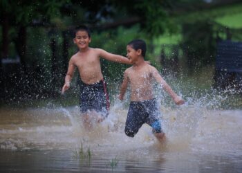 DUA kanak-kanak kelihat gembira bermain air semasa banjir melanda Pasir Puteh pada Disember lalu.-UTUSAN/KAMARUL BISMI KAMARUZAMAN