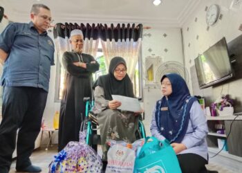 FARIHAH Che Husin (kanan) menyerahkan faedah ilat SKSSR kepada Rohaya Jalil di Kampung Bukit Gasing, Marang, Terengganu. - UTUSAN/TENGKU DANISH BAHRI TENGKU YUSOFF