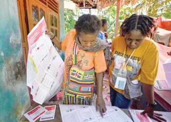 Dua pengundi wanita melihat calon-calon yang bertanding dalam Pemilihan Umum (Pemilu) Indonesia dan Pilihan Raya Presiden (Pilpres) sebelum mengundi di daerah Kwamki Narama, Papua Tengah semalam. - AFP